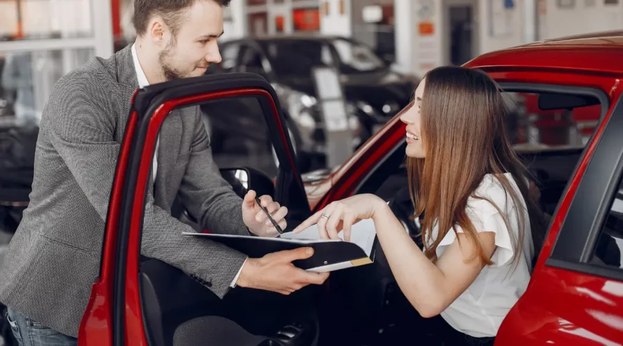 Un vendeur remet un contrat à une cliente assise dans une voiture rouge dans un concessionnaire automobile. Location de voiture au Maroc